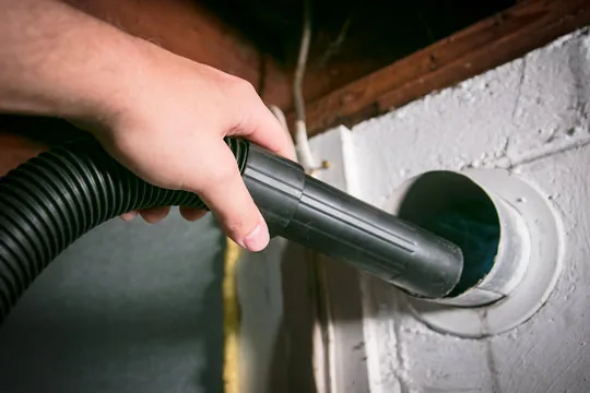 Vacuum nozzle cleaning a dryer exhaust opening in a wall