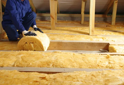 Installer unrolling fiberglass batt insulation between attic joists
